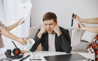 Stressed man sitting at a desk overwhelmed by multiple distractions
