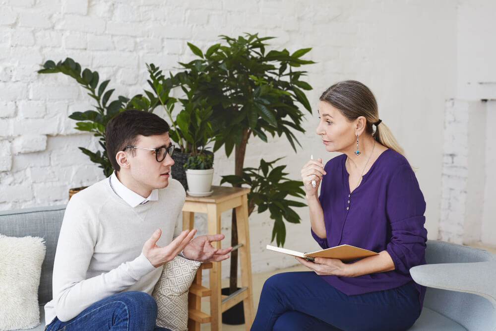 A person sitting thoughtfully in a therapy room, unsure of what to say during a counselling session.